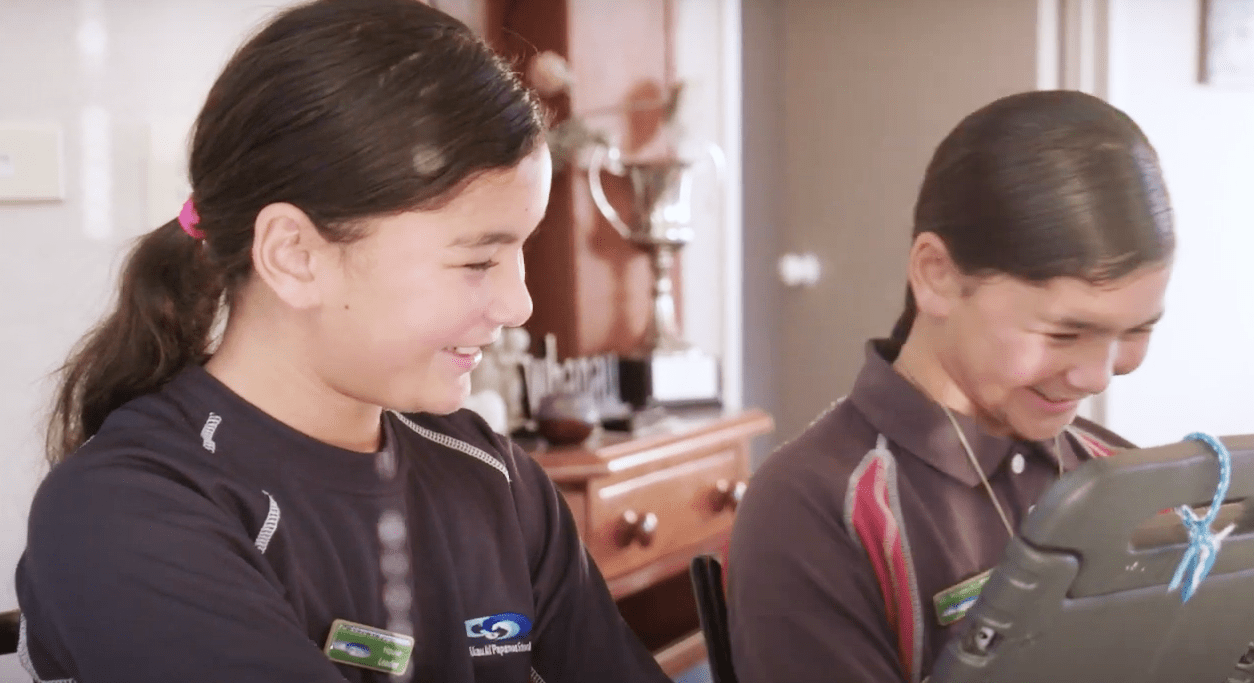 Two girls are sitting at a table and using a tablet