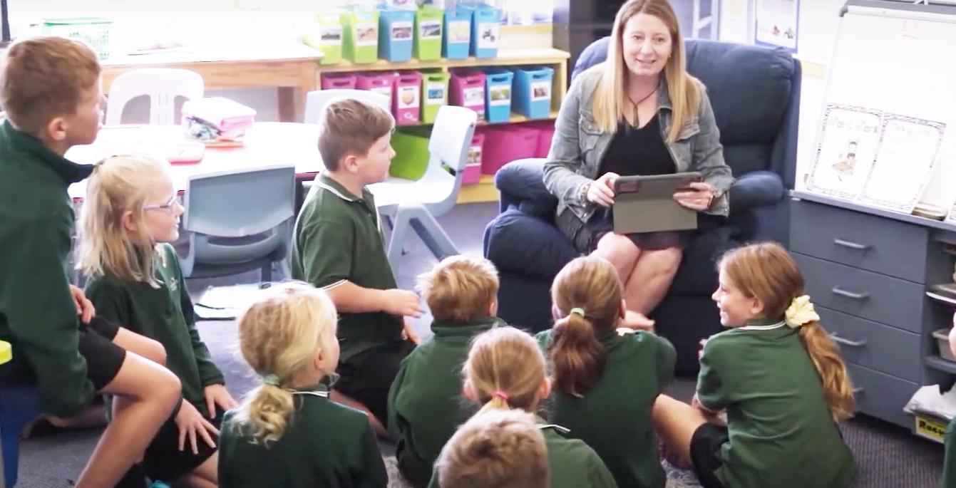 A woman teacher is sitting in front of a group of children