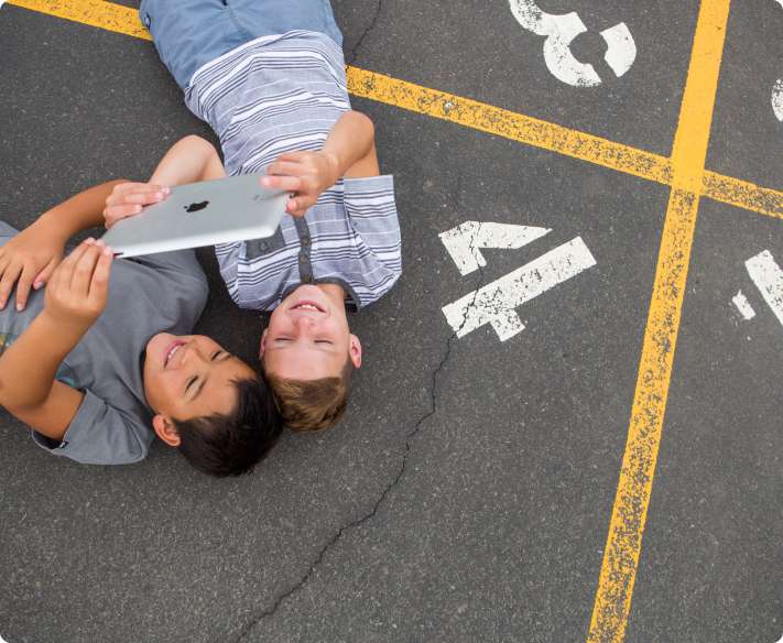 Two young boys lying on the ground looking at a tablet