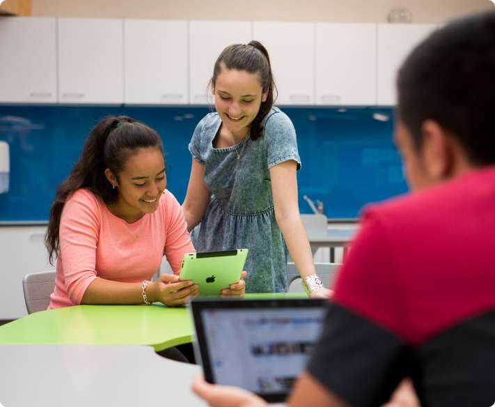 Two students smiling while looking at a tablet in the classroom