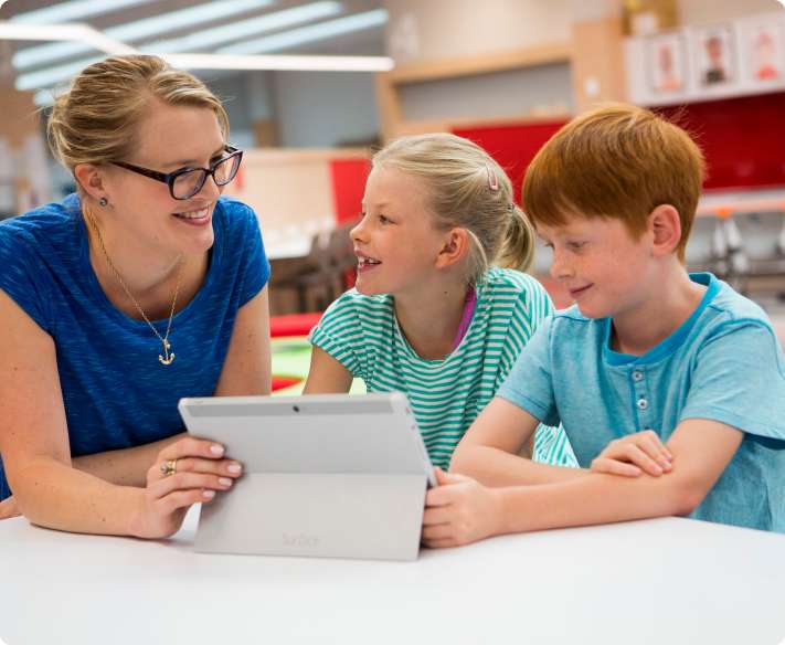 Teacher working with two students while holding tablet in a classroom