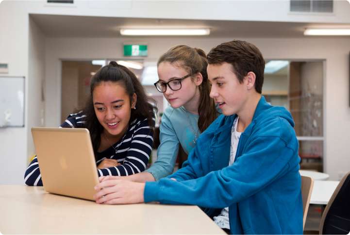 Three youth looking at a laptop on a desk