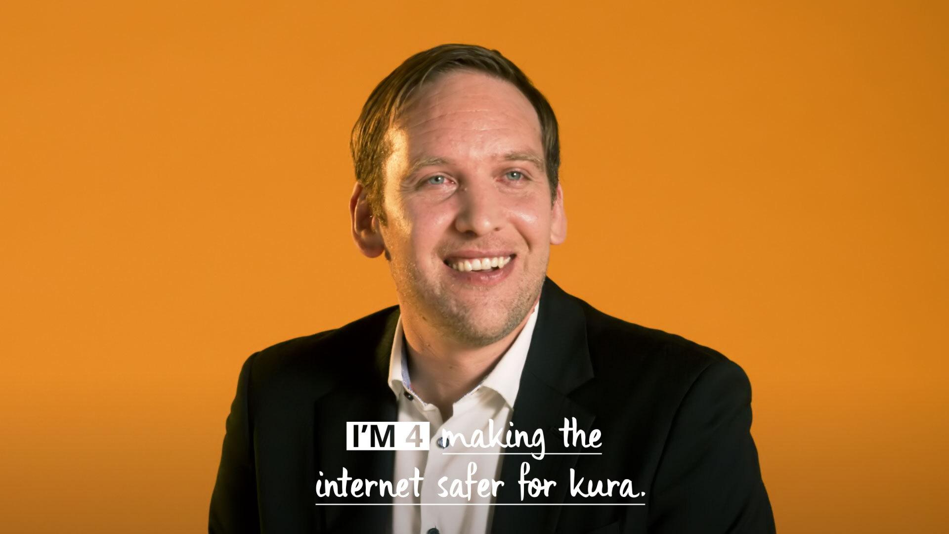 Man smiling sitting in front of an orange background with caption: I'm for making the internet safer for future kura