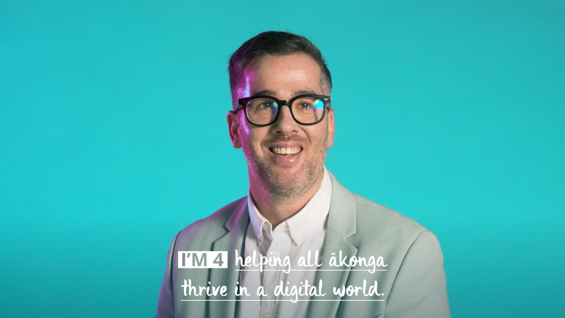 Man smiling sitting in front of a green background with caption: I'm for helping all akonga thrive in a digital world