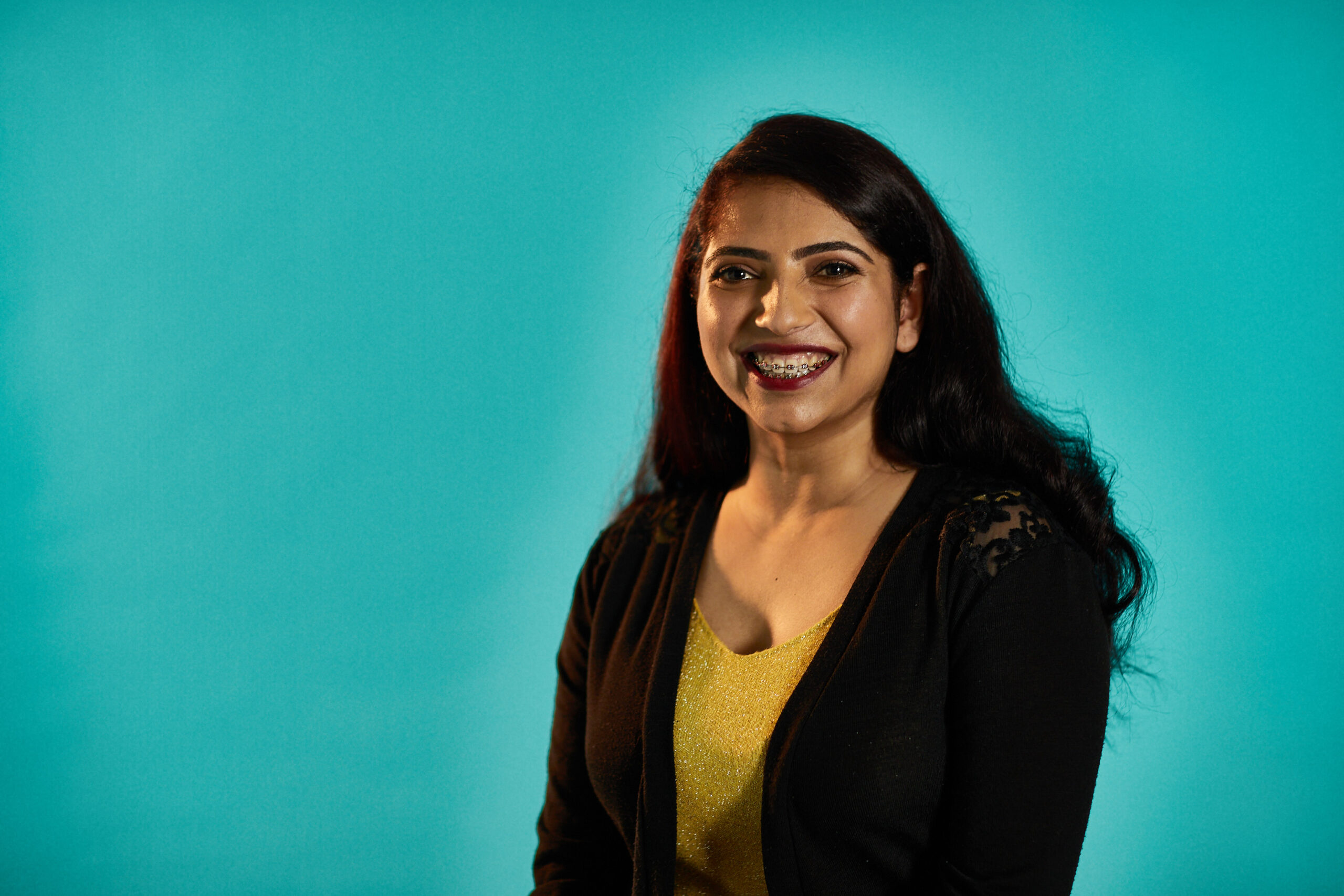 Woman smiling sitting in front of a teal background