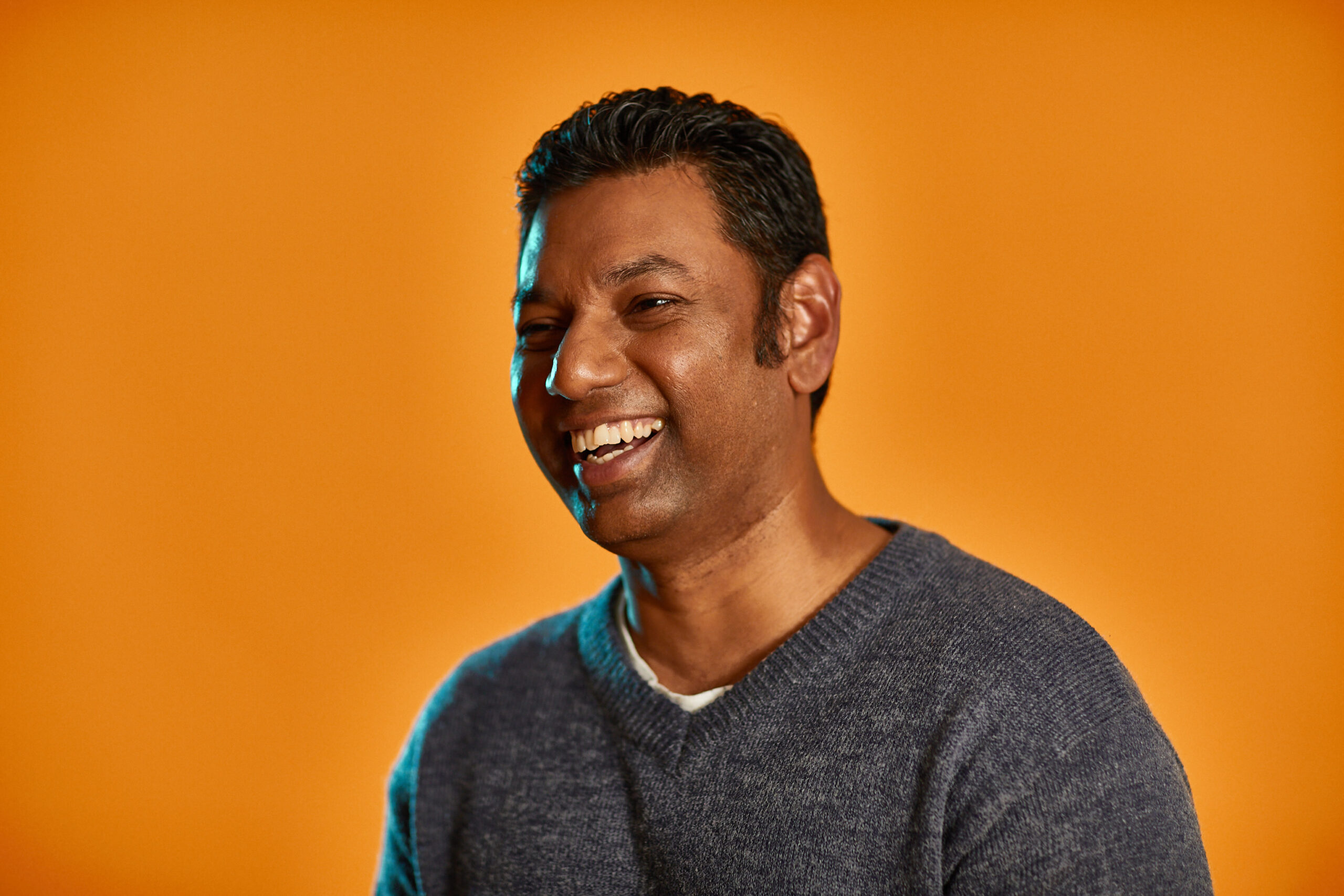 Man smiling sitting in front of an orange background