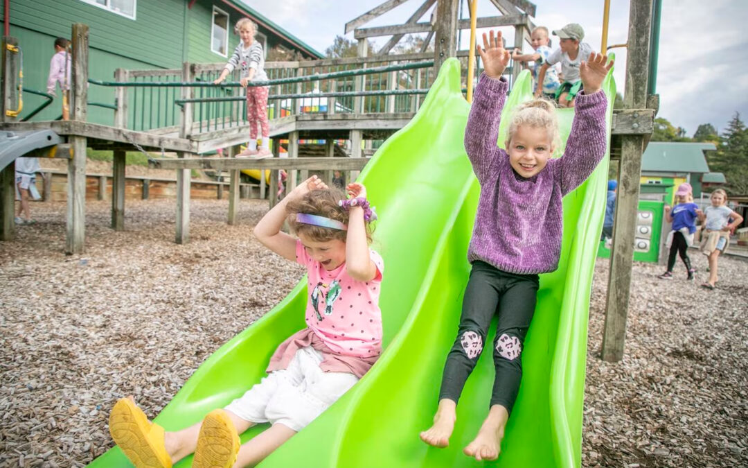 Two girls on green slide in playground