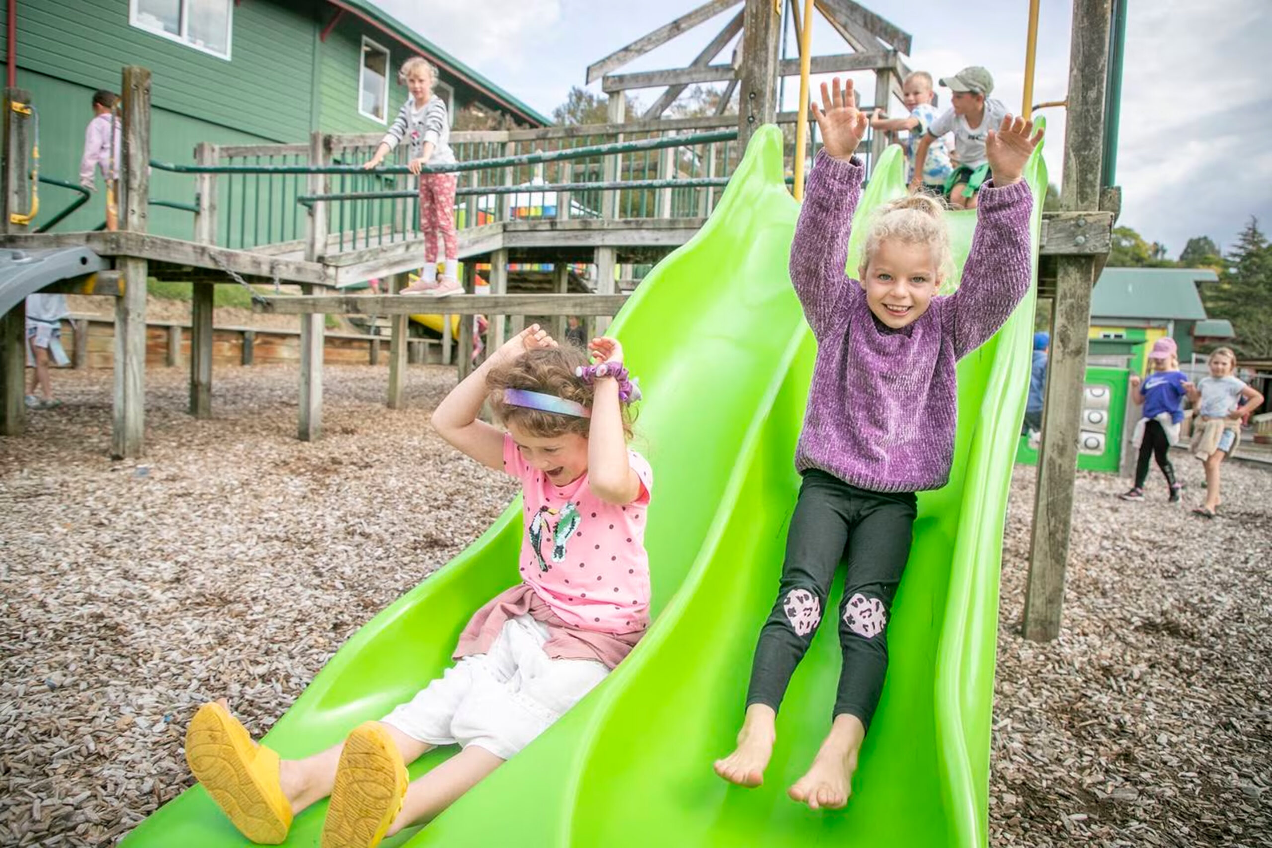 Two girls on green slide in playground