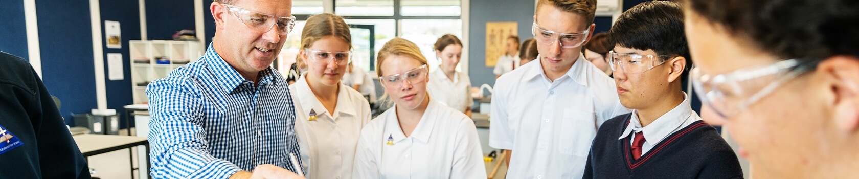 A group of students with a teacher conducting an experiment all wearing goggles