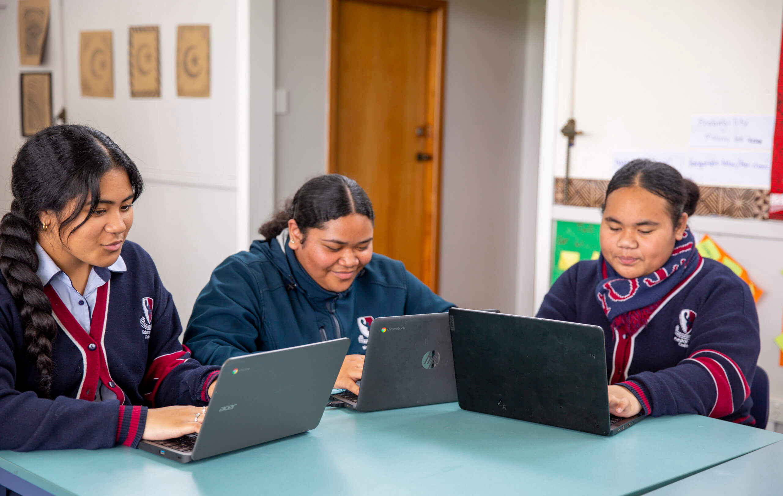 A group of girls are sitting at a table using a laptops