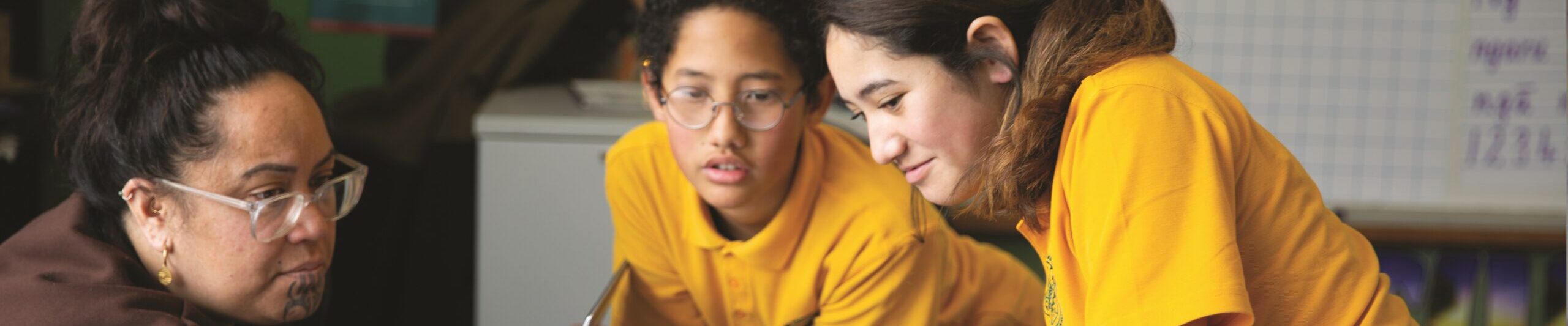 Teacher in classroom with two kids in front of laptop